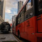 Ônibus urbano vermelho parado em uma estação moderna no centro de Curitiba.