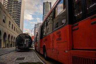 Ônibus urbano vermelho parado em uma estação moderna no centro de Curitiba.