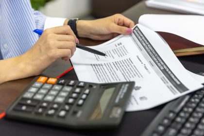 Pessoa analisa documentos financeiros com calculadora e caneta sobre uma mesa.