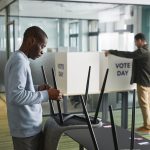 Dois homens preparam cabines de votação em uma seção eleitoral interna.