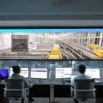Pessoas monitoram sistemas e grandes painéis digitais em uma moderna sala de controle.