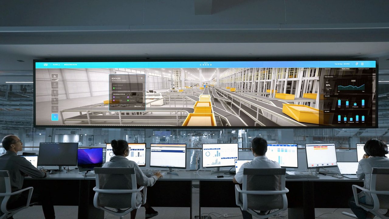 Pessoas monitoram sistemas e grandes painéis digitais em uma moderna sala de controle.