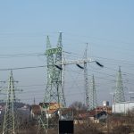 Linhas de alta tensão e torres de transmissão de energia em área urbana sob céu azul.