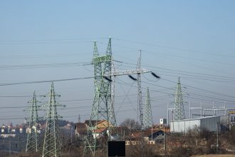 Linhas de alta tensão e torres de transmissão de energia em área urbana sob céu azul.