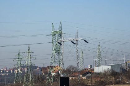 Linhas de alta tensão e torres de transmissão de energia em área urbana sob céu azul.