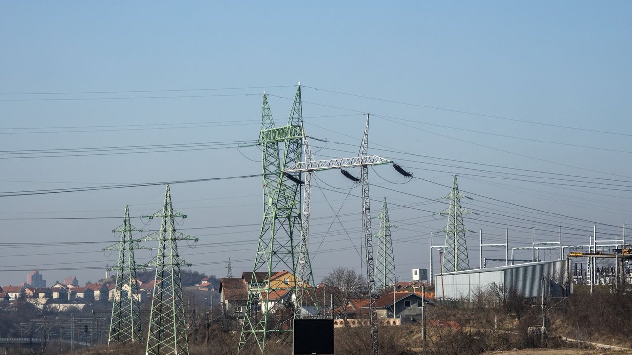 Linhas de alta tensão e torres de transmissão de energia em área urbana sob céu azul.