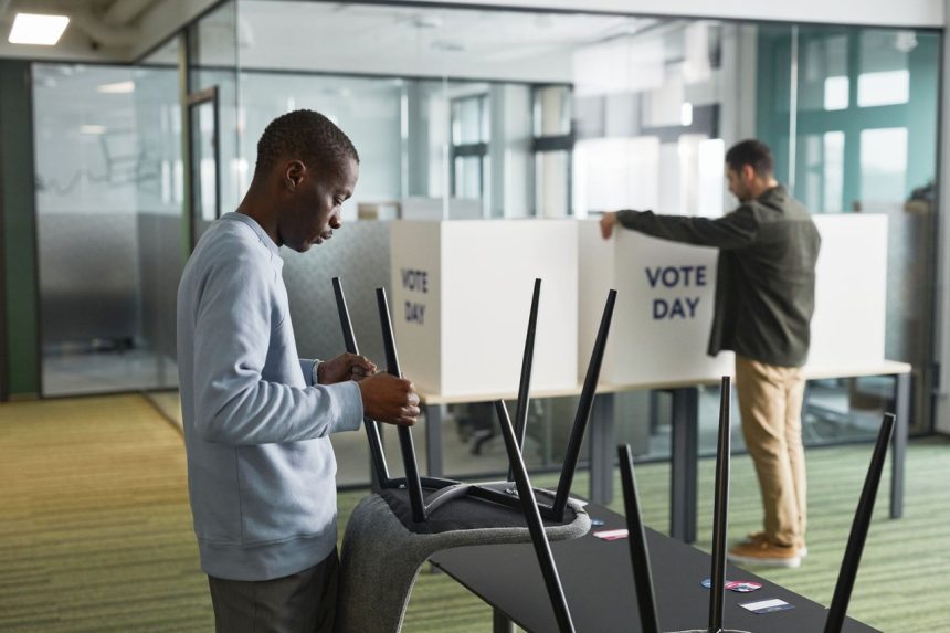 Dois homens preparam cabines de votação em uma seção eleitoral interna.