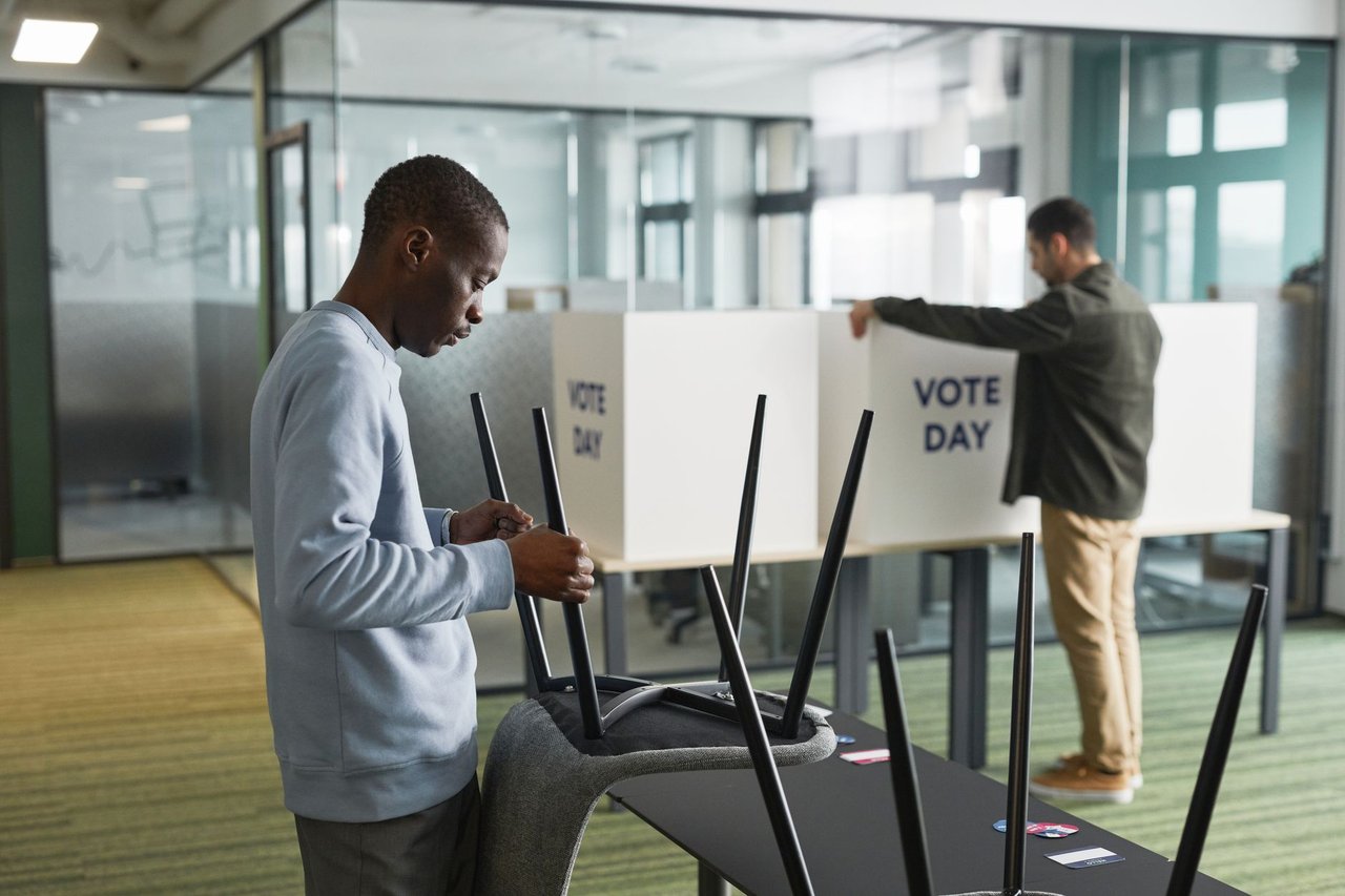 Dois homens preparam cabines de votação em uma seção eleitoral interna.